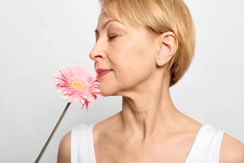 Woman smelling a flower in spring, beauty and skincare wellness concept, nature freshness, calm portrait, eyes closed, pink blossom, studio white background