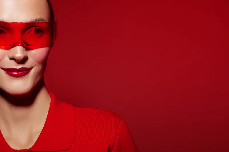 Close-up of a woman wearing red sunglasses and a red top against a red background. Concept of fashion, style, confidence, and modern minimalism with vibrant color contrast.