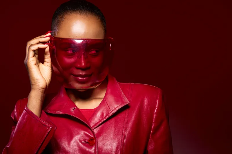 Portrait of dark skinned African woman wearing red leather jacket and red transparent visor on red background. Fashion concept with confident model in bold color styling and accessories.
