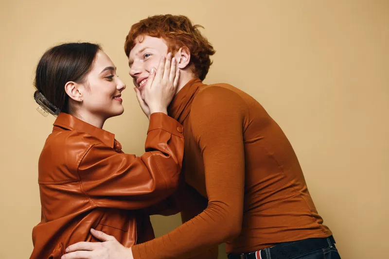 Couple, love, affection, and intimacy with young man and woman touching faces in warm clothing. Romantic relationship, casual lifestyle, and comfortable moment at indoor studio setting.