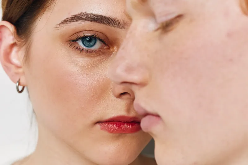 Closeup of two faces with focus on a female blue eye and natural skin texture. Woman and man with serious expression for portrait, emotions and human connection indoors.