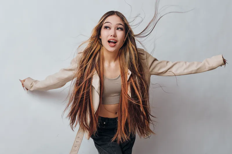 Young woman with long straight hair wearing casual outfit posing with arms extended isolated on white background. Studio portrait of happy girl with natural makeup and energetic expression.