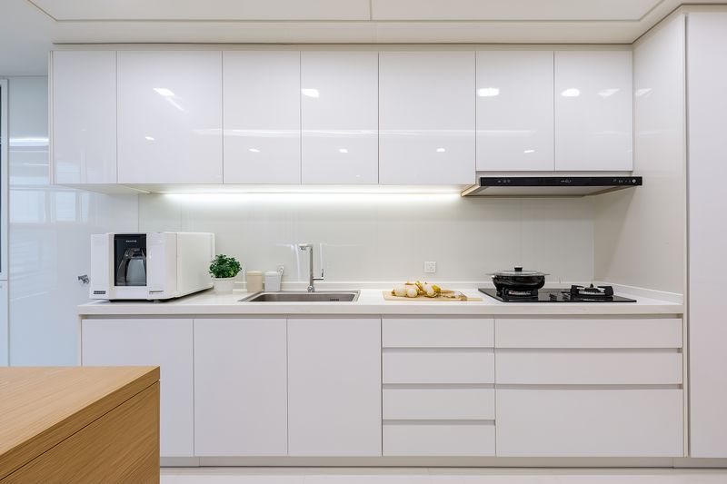 Bright minimalist modern kitchen interior with glossy white cabinetry, integrated appliances and clean quartz countertops, featuring undercabinet LED lighting, subtle decor and neutral contemporary