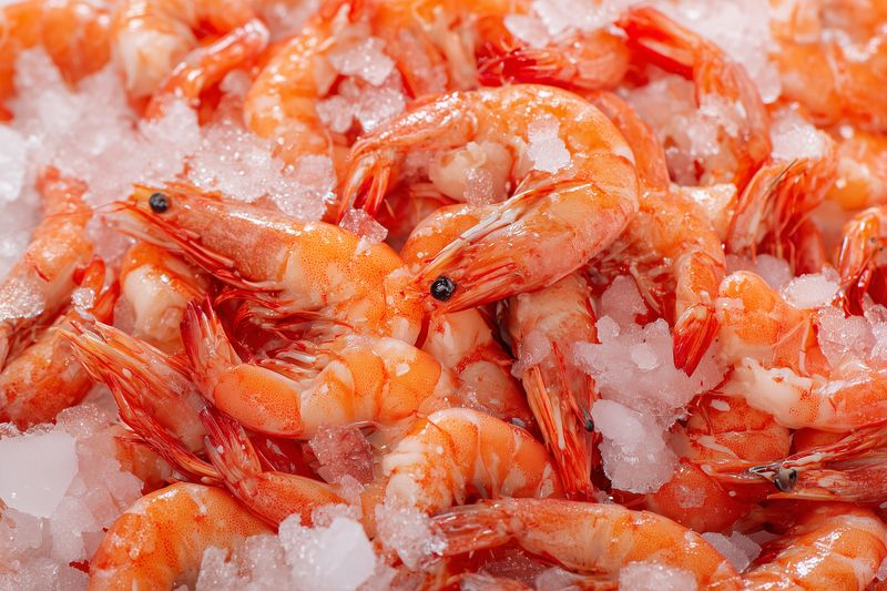 Close-up of fresh cooked shrimp piled on crushed ice, showcasing vibrant orange shells and glistening texture, ideal for seafood market and food preparation.