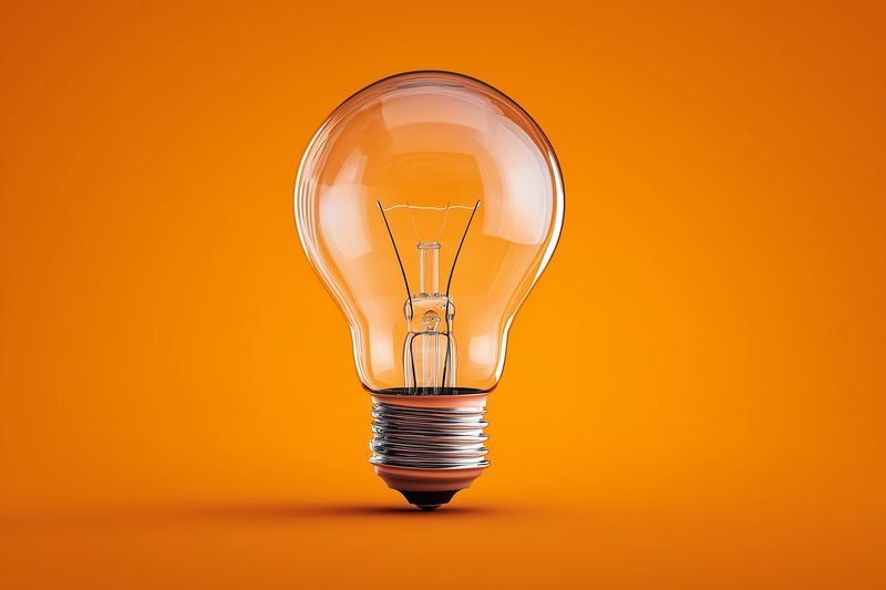 A clear incandescent light bulb against a vivid orange background, symbolizing creativity, bright ideas, innovation and energy in modern design, photography and visual communication.
