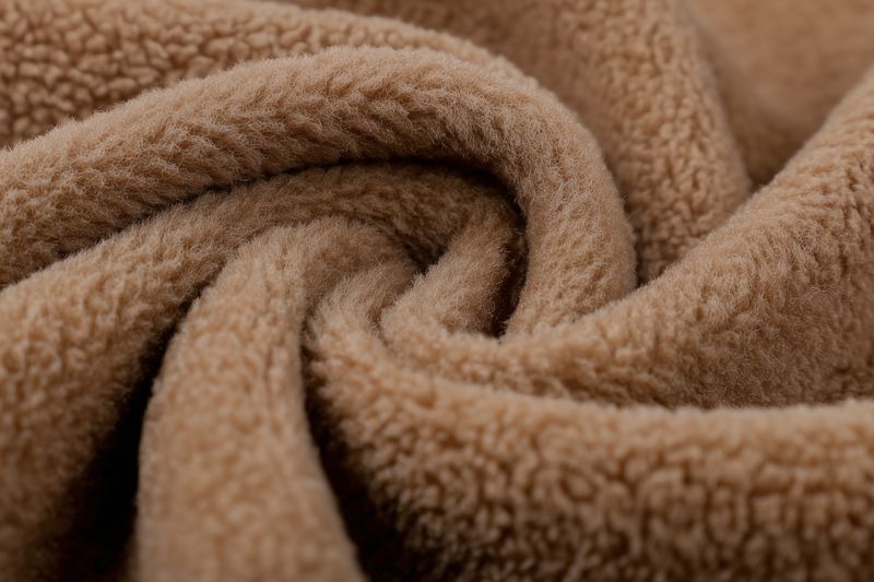 Close-up of soft brown fleece fabric showing plush texture and curled folds, creating a warm, cozy and tactile abstract pattern, ideal for backgrounds, textiles and seasonal design.