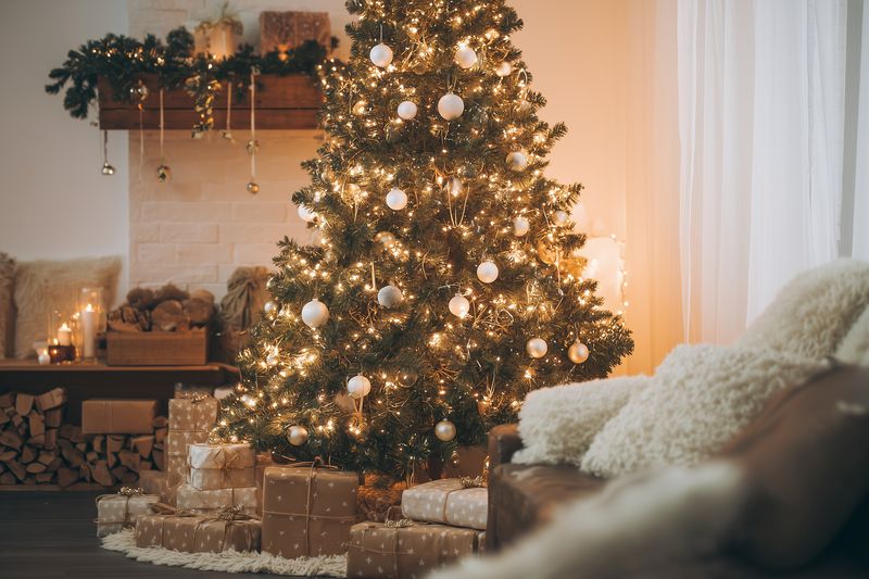 Cozy living room featuring a decorated Christmas tree glowing with warm fairy lights and white ornaments, surrounded by neatly wrapped gifts and a lit fireplace for a festive atmosphere.