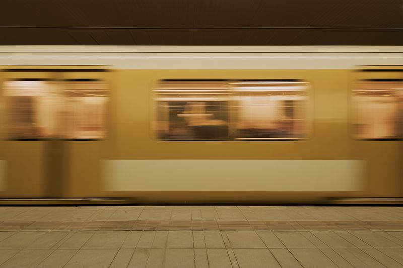 Motion blur of a yellow subway train passing through an underground platform, capturing speed and urban transit atmosphere with blurred passengers and warm interior lights.