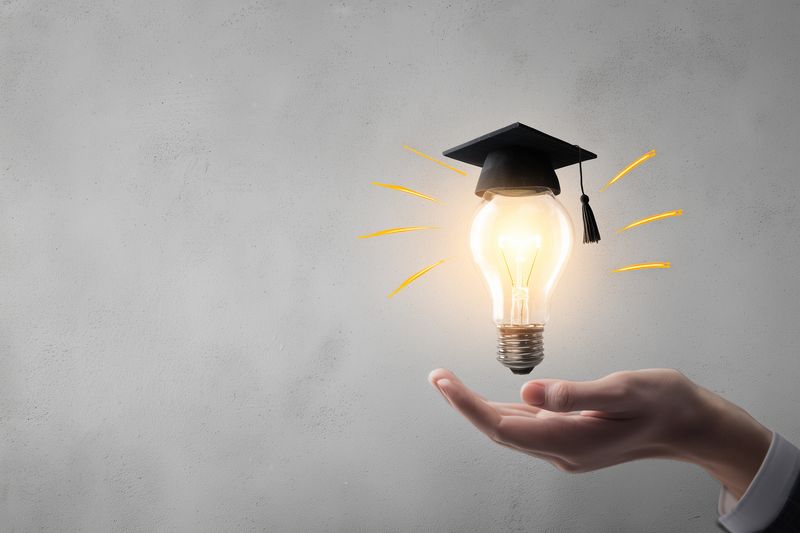 Bright glowing light bulb wearing a graduation cap floating above an outstretched hand, symbolizing academic achievement, creative thinking, innovation and the spark of new educational ideas.