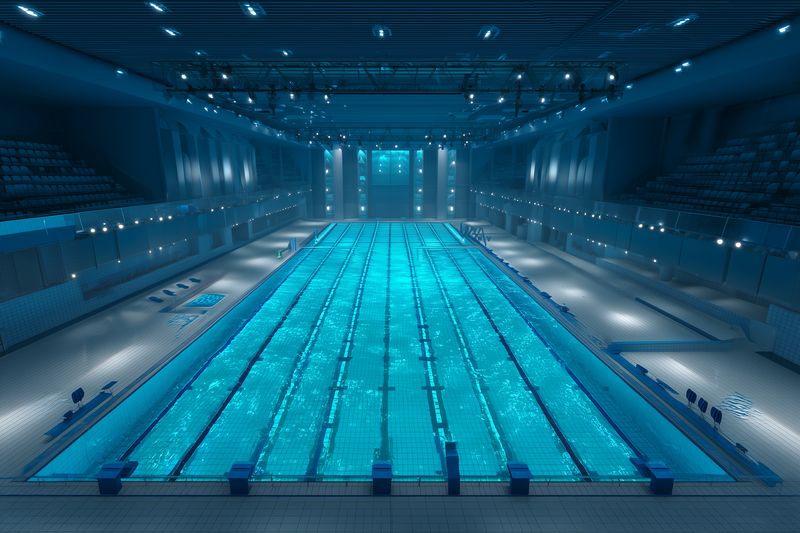 Empty indoor competition swimming pool with illuminated blue lanes and reflective water surface. Modern architecture, tiled deck and starting blocks under ambient ceiling lighting, calm and pristine.