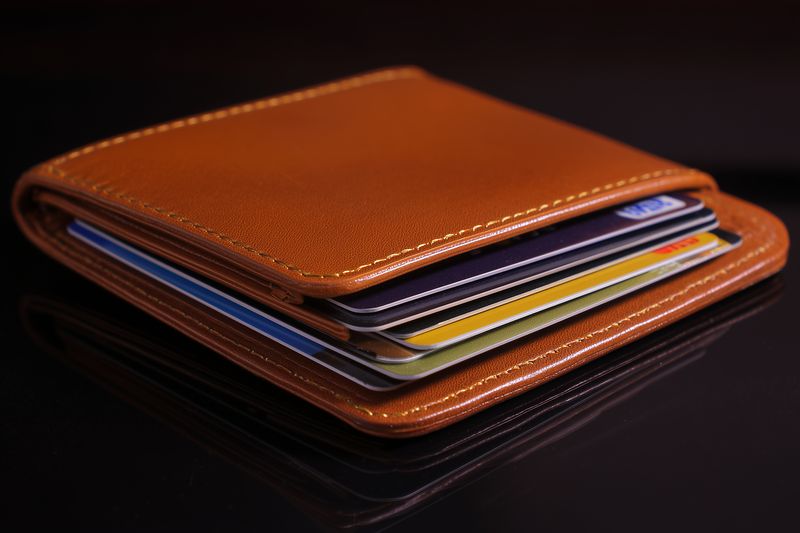 Close-up of a brown leather wallet packed with multiple cards and credit cards, resting on a glossy black surface, highlighting texture, stitching and compact organized design.