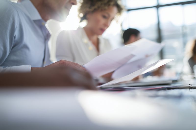 Business team members reviewing documents at a modern office meeting table, focused on paperwork and collaboration, shallow depth of field and natural light creating a professional atmosphere.