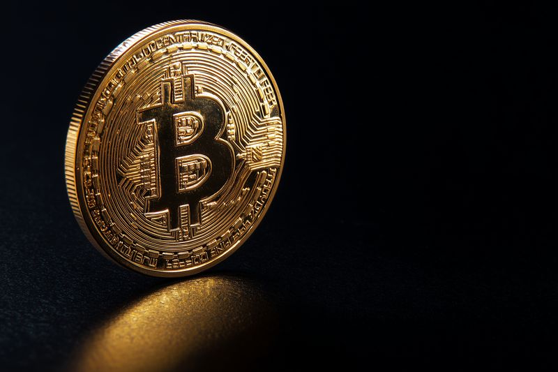 Close-up of a shiny golden cryptocurrency coin standing on a reflective dark surface, detailed circuitry pattern and prominent currency symbol suggesting digital finance and investment.