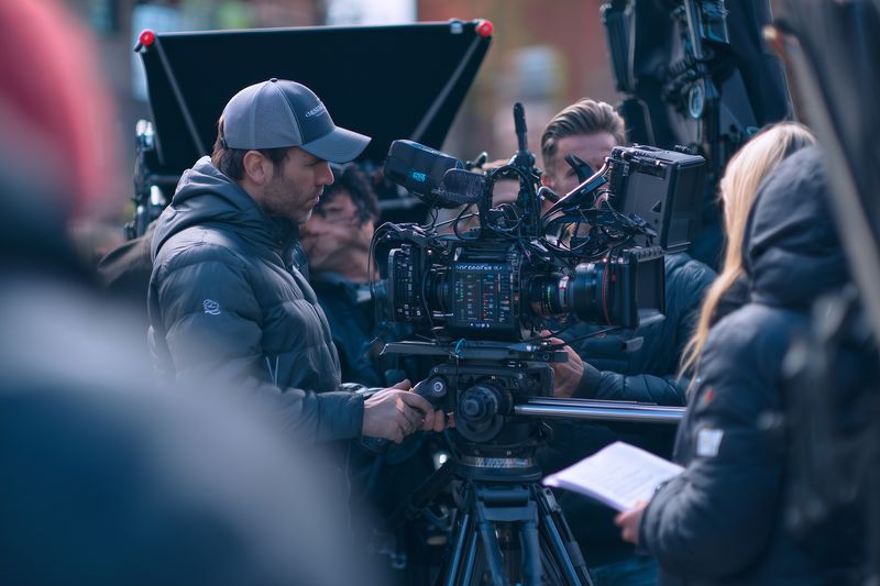 A professional film crew operates a large cinema camera on set, coordinating focus, framing and movement while technicians monitor equipment and lighting to capture cinematic visuals.