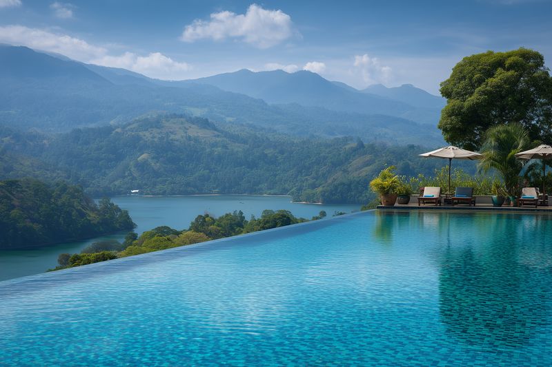 Infinity pool overlooking a tranquil lake and layered mountain ranges, with lounge chairs and umbrellas on a terrace, lush greenery and misty blue horizons.