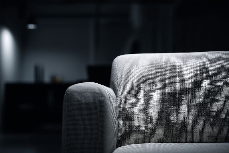 Close-up of a gray fabric sofa armrest in a dim modern living room, highlighting textured upholstery and minimalist design elements that suggest comfort, warmth and contemporary home style.