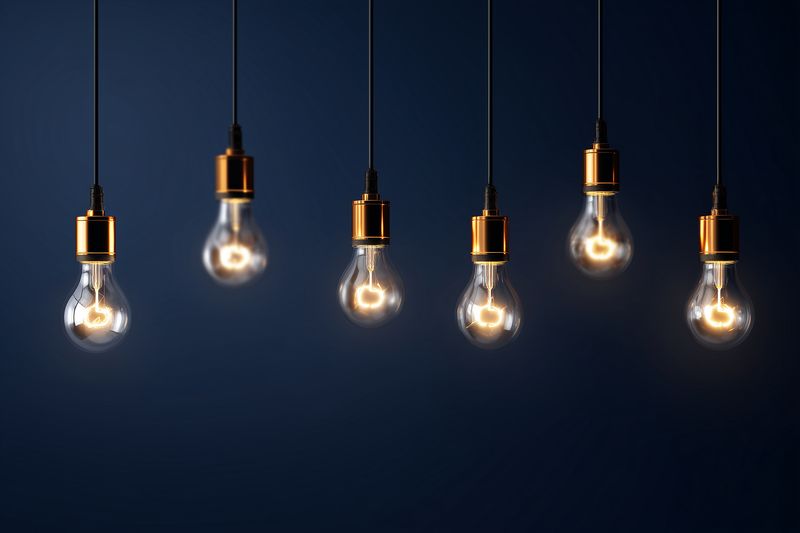 Row of glowing hanging light bulbs with warm filament glow against a dark background, minimalist composition conveying ideas of creativity, innovation and energy in lighting.