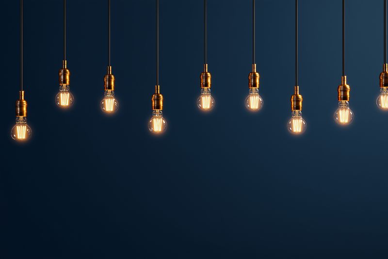 A row of hanging vintage filament light bulbs suspended from cords against a deep blue background, casting warm ambient glow and soft shadows for an industrial minimalist aesthetic.