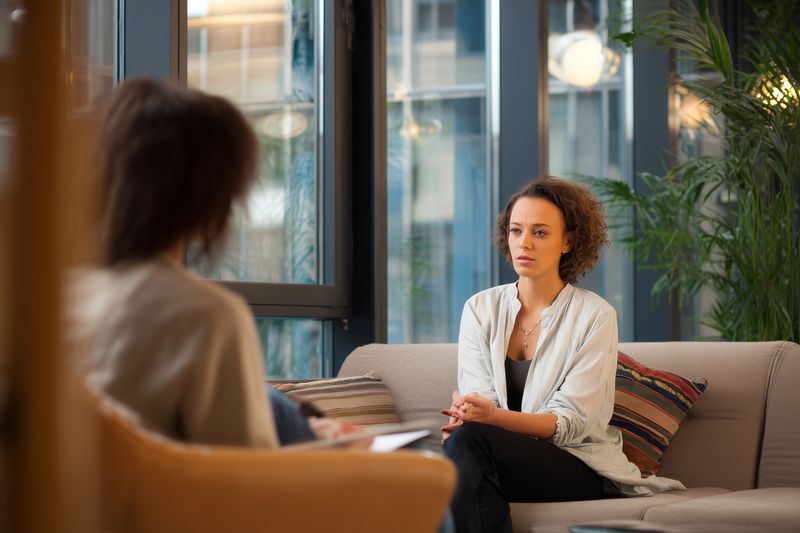 Young woman in a relaxed modern office consulting with a therapist during a one-on-one counseling session, attentive listening, supportive conversation and emotional wellbeing.