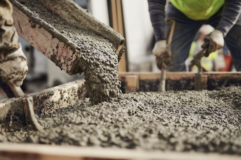 Close-up of fresh concrete being poured and spread on a construction site as workers in safety gear level and smooth the wet mixture for a new foundation or slab during building work.