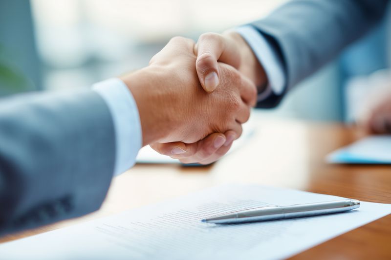 Successful business handshake between two professionals over a signed contract on a wooden desk, symbolizing agreement, partnership, deal closing and corporate collaboration.