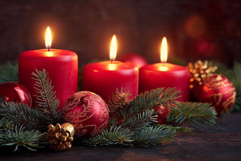 Three glowing red pillar candles surrounded by evergreen branches, glittering baubles and golden pine cones on a rustic wooden table, evoking warm holiday ambiance and festive mood.