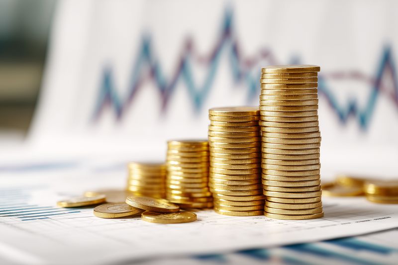 Close-up of stacked gold coins on financial reports and charts, representing investment growth, savings, capital accumulation, profit analysis and economic success for business finance.