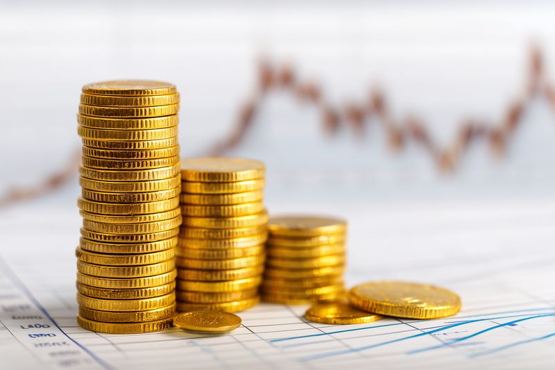 Stacked gold coins on financial charts symbolizing wealth accumulation, investment growth and economic success. Blurred stock graph in background conveys market trends.