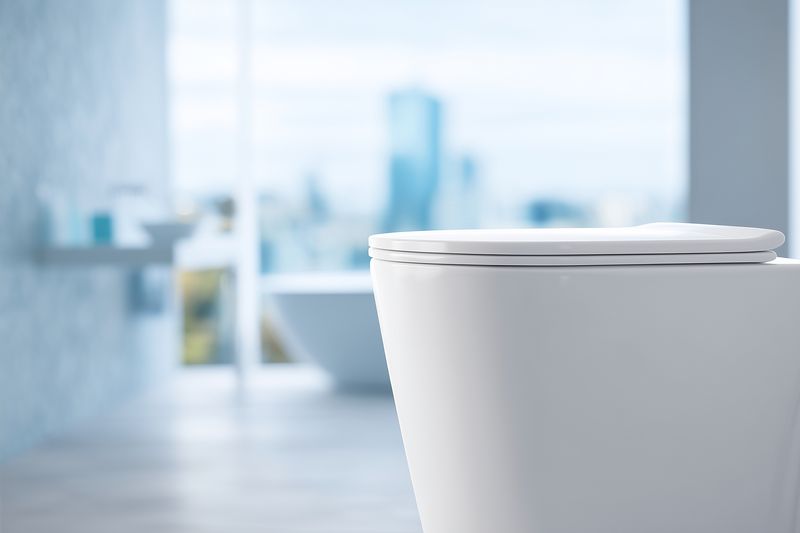 Close-up of a modern white toilet with closed lid in a bright minimalist bathroom, shallow depth of field highlighting clean ceramic lines and contemporary sanitary fixture design.