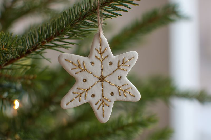 Close-up of a handmade white star ornament with gold glitter hanging on a fresh evergreen branch, creating a warm festive atmosphere and cozy holiday decor in soft natural light.