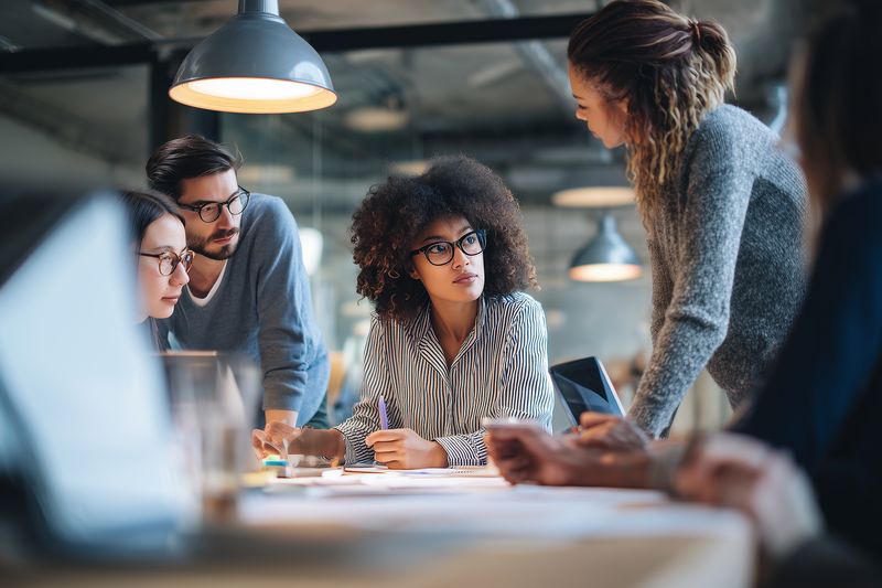 Diverse team of professionals collaborating around a table in a modern office, discussing ideas, planning projects and brainstorming during a focused creative meeting.