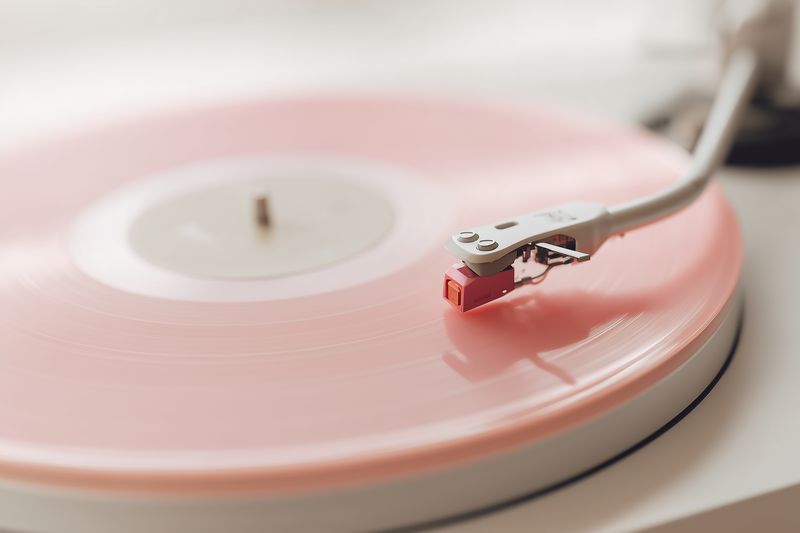 Close-up of a pastel pink vinyl record spinning on a vintage turntable, highlighting the tonearm and stylus with soft lighting, evoking nostalgic and elegant analog music.