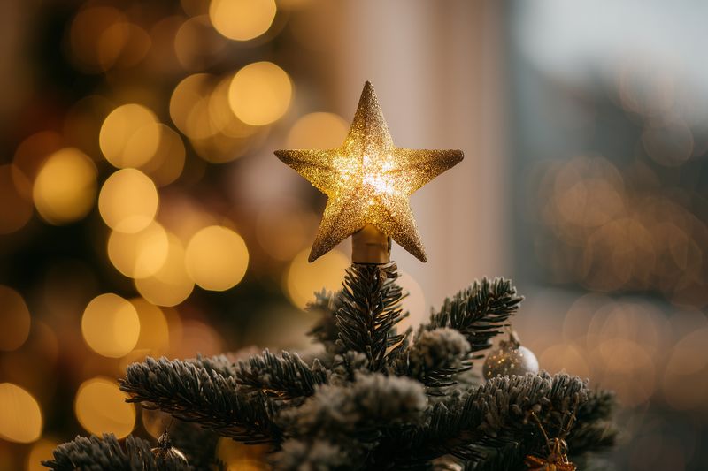 Glittering star tree topper perched on a snow-dusted evergreen branch, glowing warmly against soft golden bokeh lights, capturing festive holiday ambiance and cozy winter celebration mood.