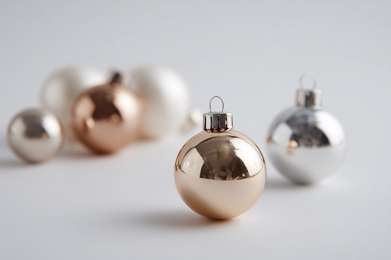 Minimal holiday ornaments in gold, silver and white arranged on a clean white background, festive reflective baubles creating an elegant seasonal still life with soft lighting.