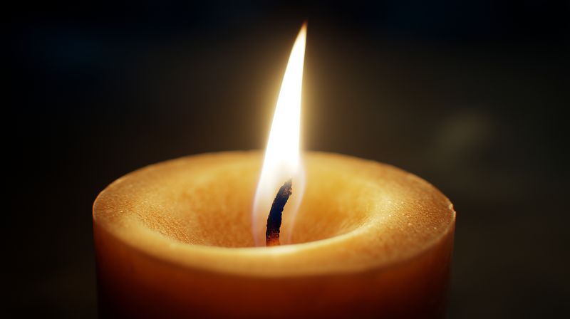 Close-up of a glowing candle flame illuminating warm textured wax in a dark setting, creating a serene intimate mood with soft highlights around the slowly flickering wick.