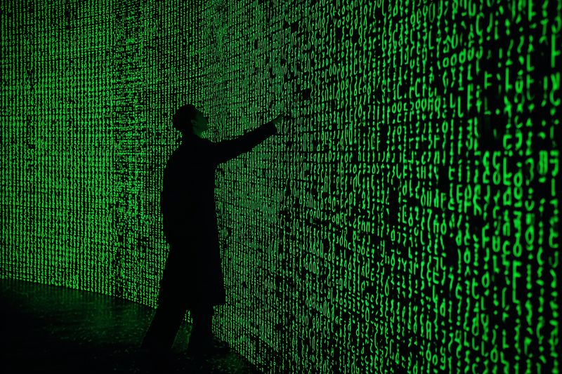 Silhouette of a person interacting with an illuminated wall of glowing green code and binary digits, evoking digital data streams, cybersecurity and a futuristic virtual environment.