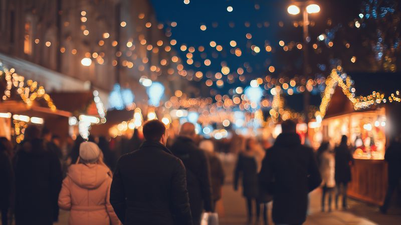 Crowded evening market scene with warm festive lights and blurred bokeh, people strolling between illuminated stalls. Cozy winter atmosphere evokes holiday cheer.