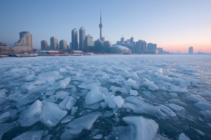 Skyline frozen city waterfront ice winter harbor dawn, buildings and tower at cold sunrise, floating ice floes on sea, pastel sky and urban landscape, serene