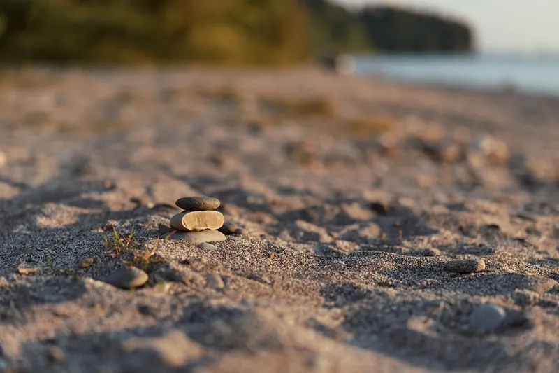 Balanced stone cairn rests on a sandy beach at sunset, creating a peaceful scene for meditation and relaxation near the calm water on a warm summer evening.