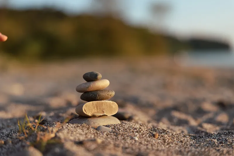 Stacked stones balancing on a sandy beach during sunset, creating a zen atmosphere of relaxation. This serene scene captures the essence of mindfulness, harmony, peace, and spiritual wellness.