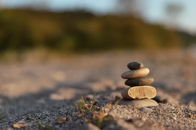Balanced stone pyramid sits on sandy beach at sunset, reflecting zen peace and tranquility, creating a meditative focus point for lifestyle wellness and spiritual harmony concepts.