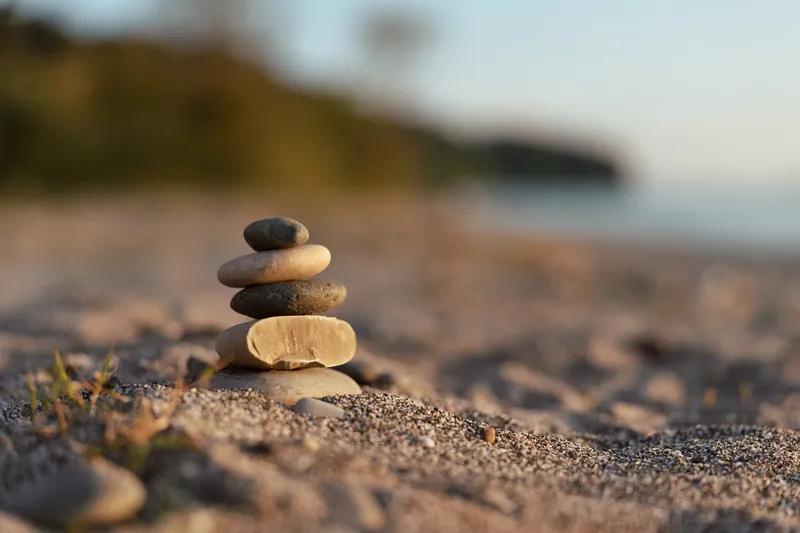 Balanced stone cairn tower stands on the sandy beach during sunset. This zen stack of rocks creates a peaceful mood for meditation, mindfulness, and relaxation by the sea.